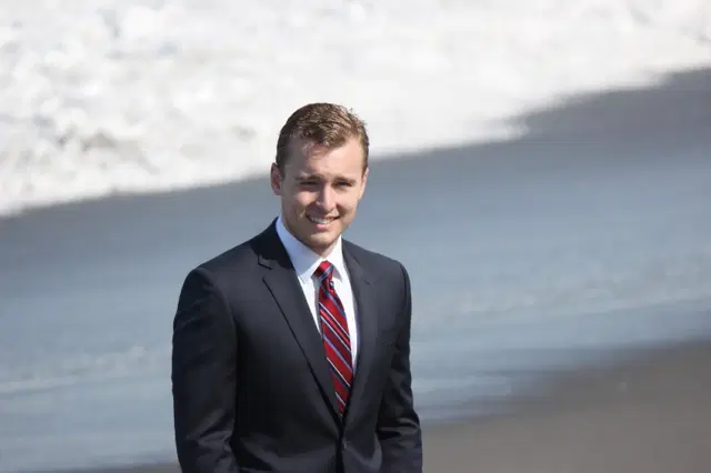 Jameson Courville in a dark suit on a beach